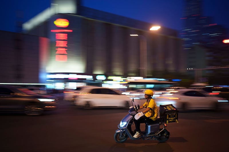 2024年7月4日,一名骑电动自行车的外卖员在傍晚时分骑电动自行车穿过北京的交叉路口。(美联社)
