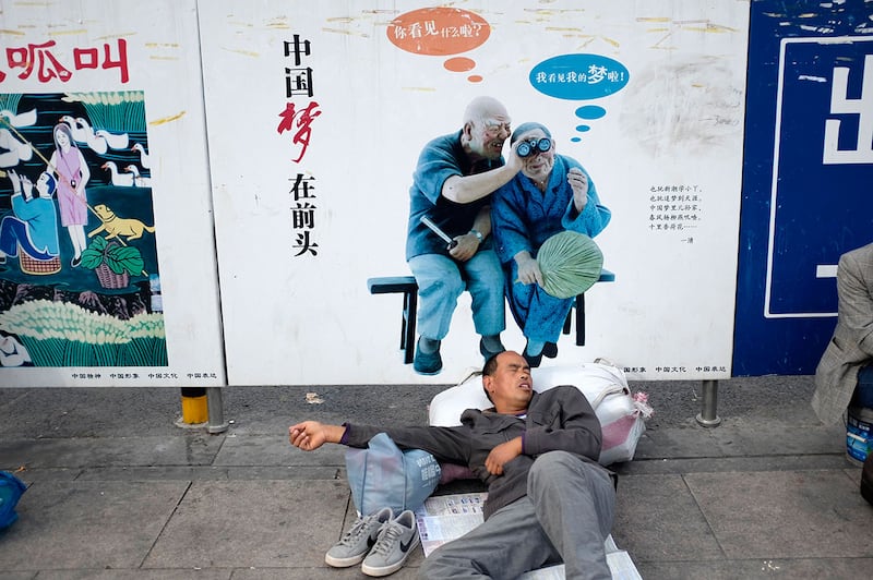 一名农民工在北京火车站一块写有“中国梦”政府宣传牌下打盹。